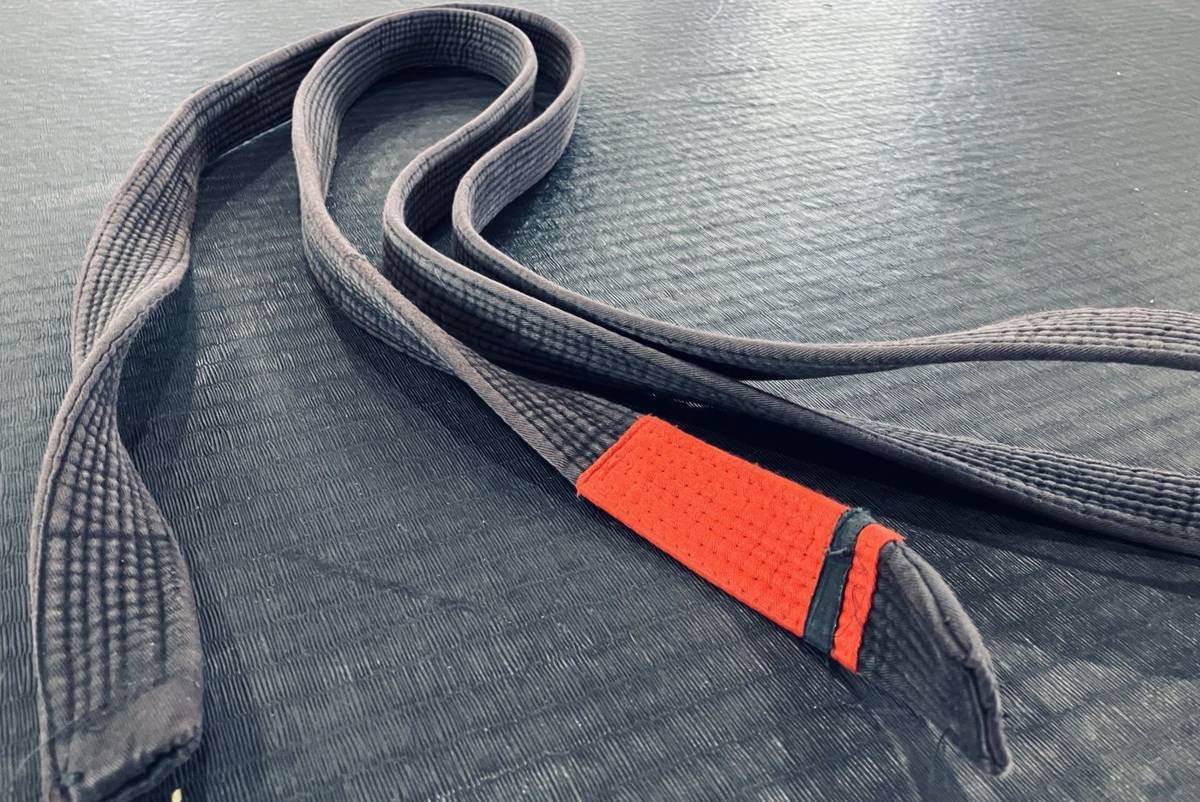 A worn black belt, faded to grey, lying on training mats